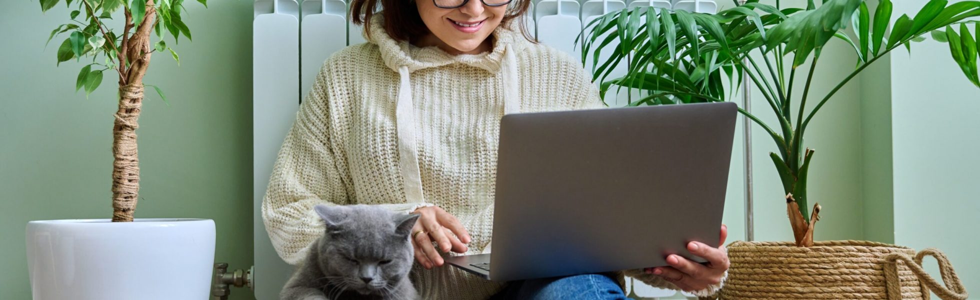 CatCary Beratung: Frau mit Britisch Kurzhaarkatze auf Schoß sitzt auf dem Boden und lächelt Laptop an